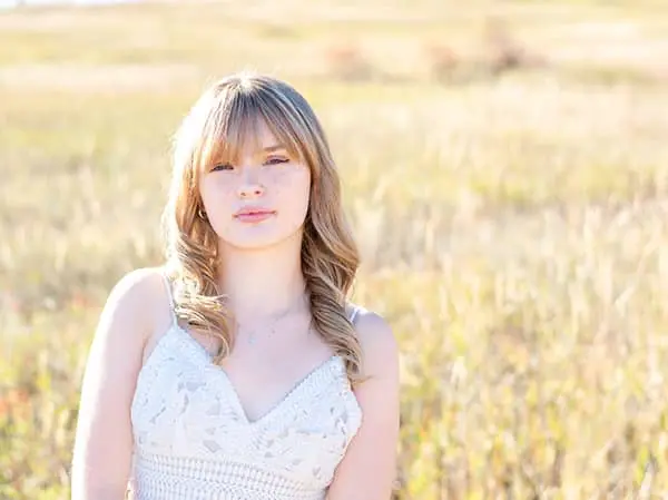 Portrait of a blonde woman in a white lace dress standing in a sunlit grassy field